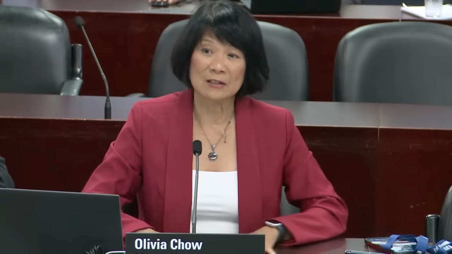 Wearing a red blazer and a white shirt, Olivia Chow speaks while seated in a Committee Room at City Hall