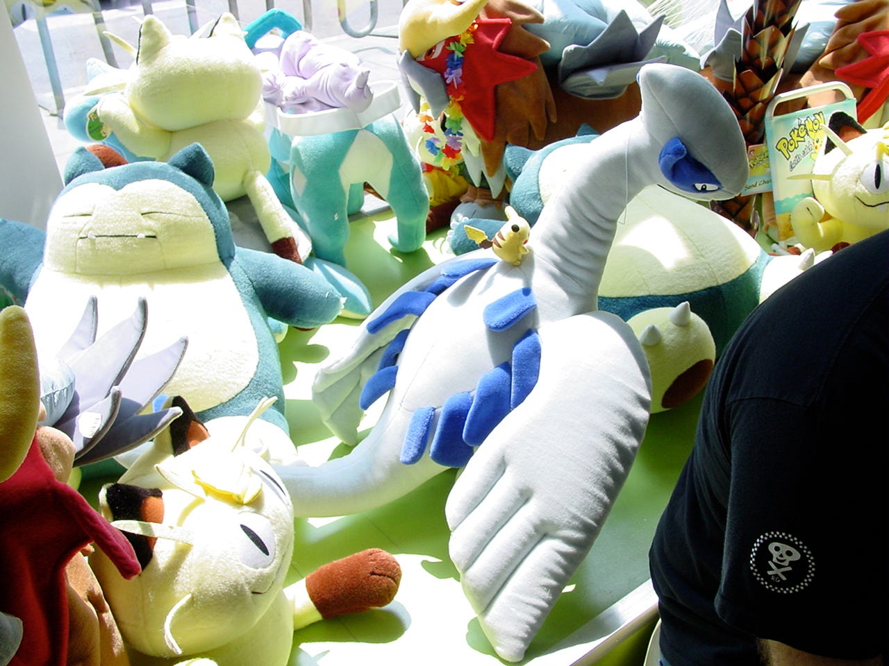 A photograph taken inside the store, showing the window display from behind. Here, we can see even more plush toys, such as Meowth, and a Pikachu on top of Lugia’s back