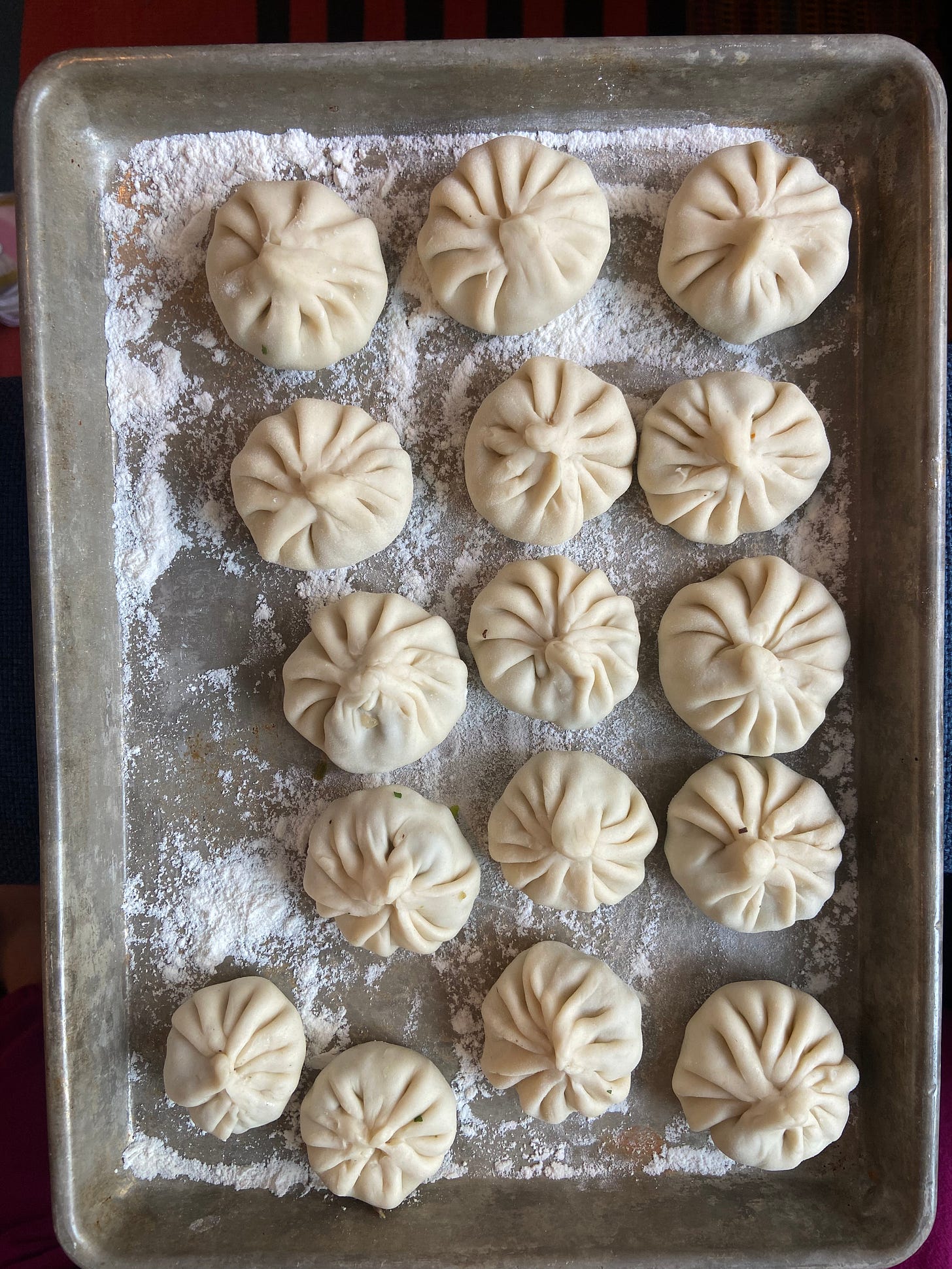 An overheard image of round pleated khinkali on a metal tray