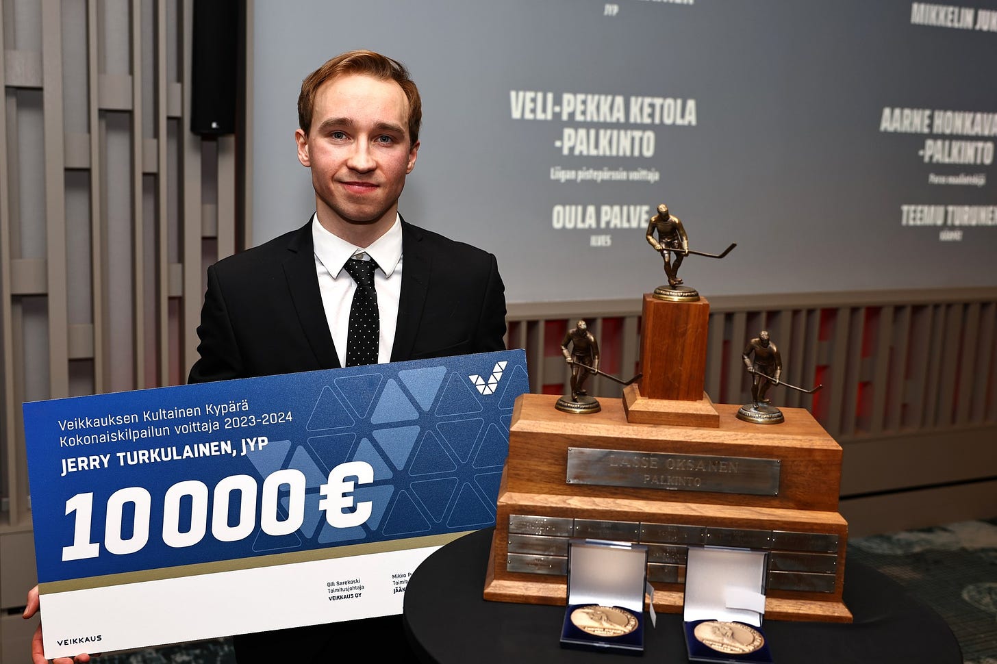 Jerry Turkulainen posing with a check and his trophies and medals during an award ceremony.