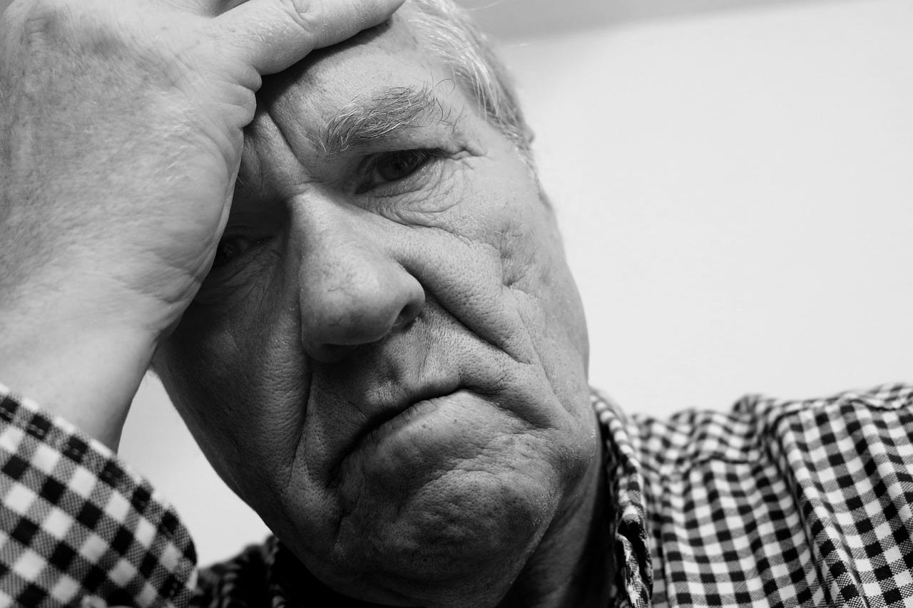 grey haired man looks frustrated as he hold his head in his hand.