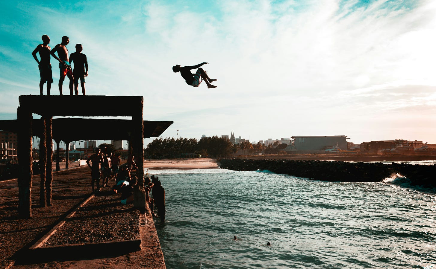 group of young men jumping off a wooden platform into the ocean at sunset