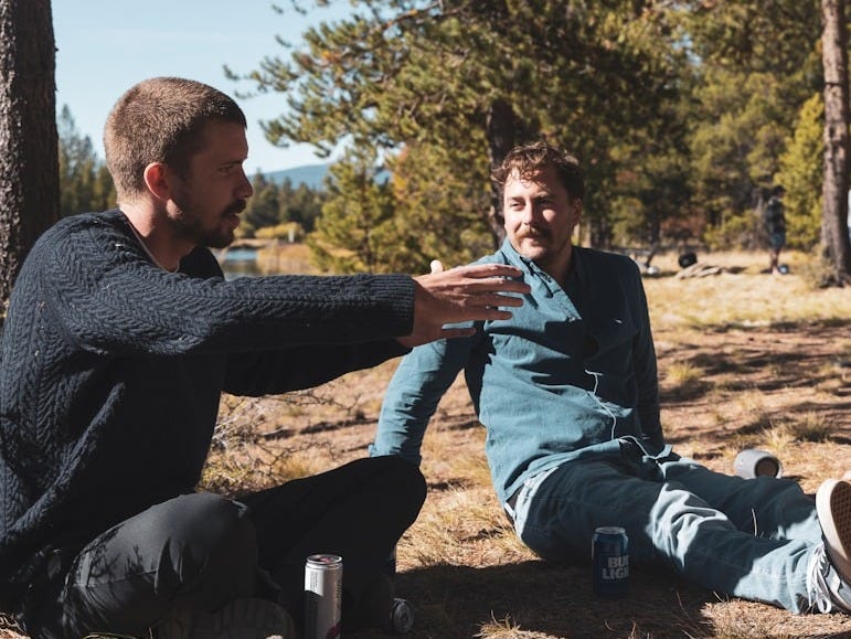 three men sitting on the ground in the woods