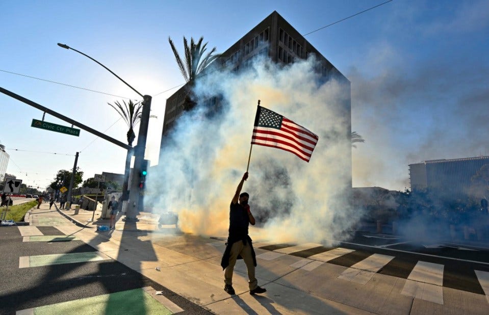 A protester raises the U.S. flag after police use tear gas and flash-bangs at the Federal Building in Santa Ana, CA, on Monday, June 9, 2025. (Jeff Gritchen/The Orange County Register via AP)