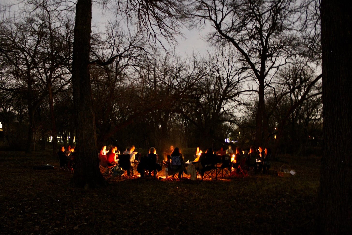 nighttime silhouettes of trees surrounding a circle of women sitting around a fire