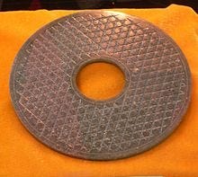 A bronze colored disk with a snake-scale pattern and a hole in the center.