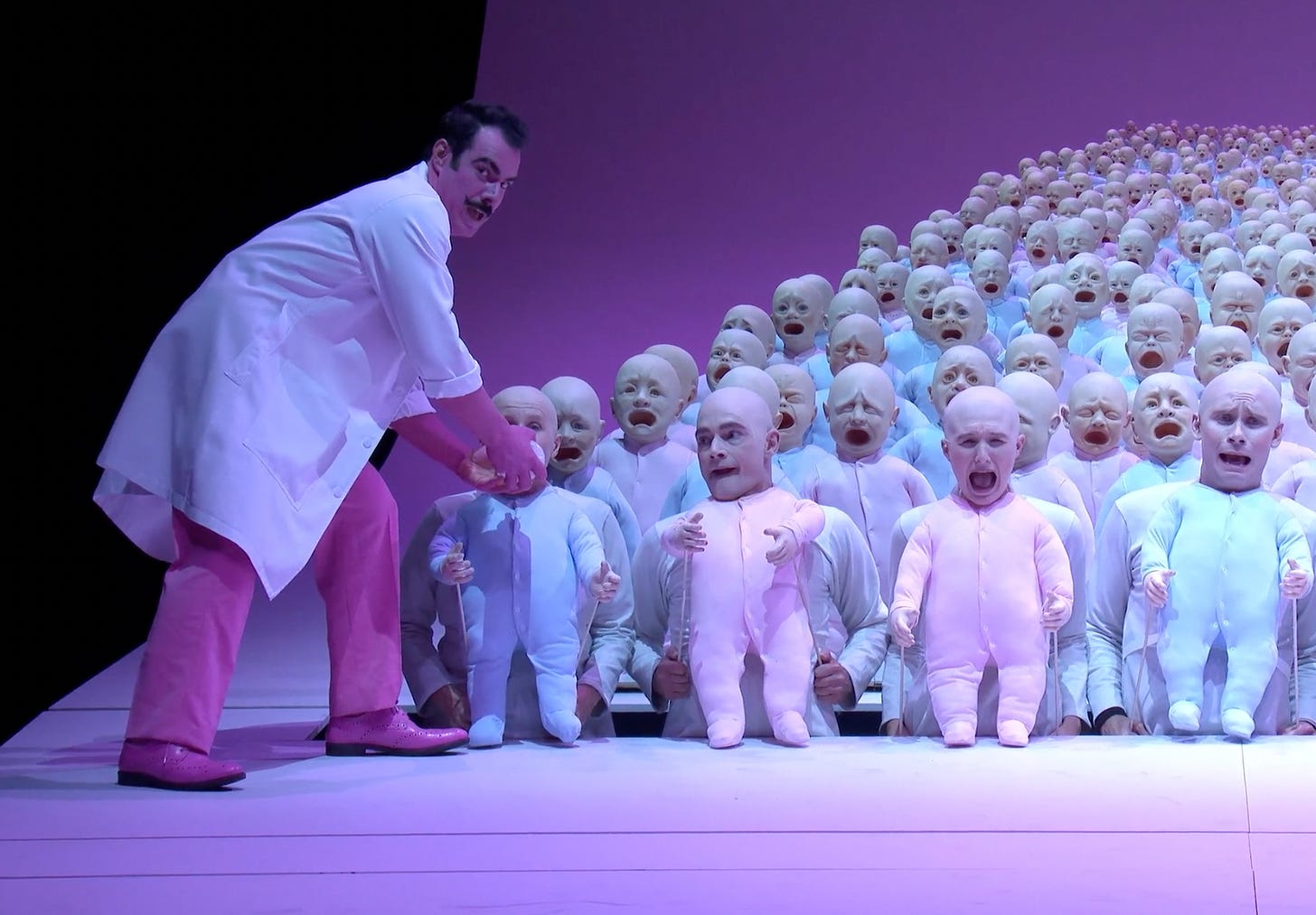 A man in a white lab coat bottle-feeds a massive crowd of babies.