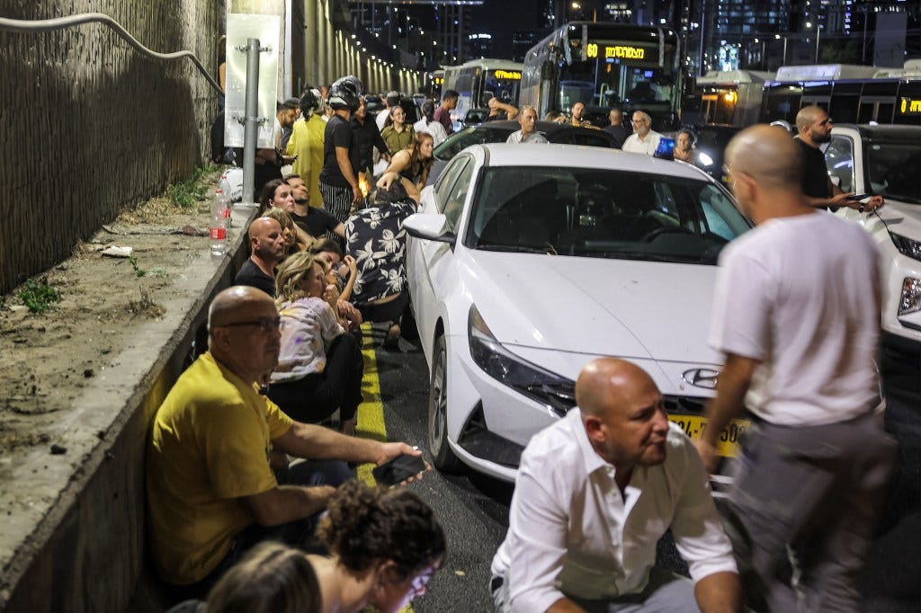 People take cover behind vehicles under a bridge along the side of a highway in Tel Aviv on October 1, 2024. 