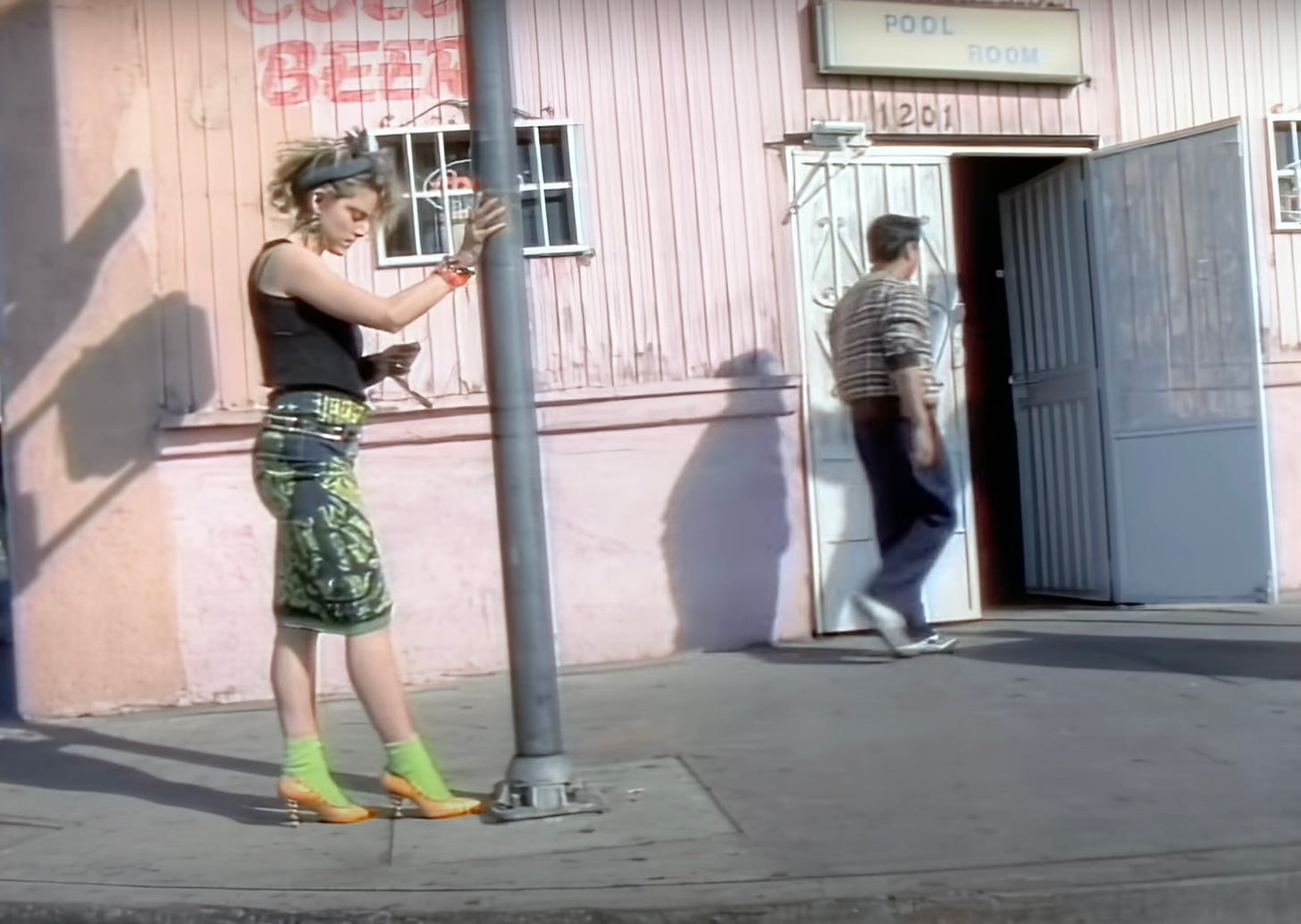 Still from the Borderline video featuring Madonna standing by a lamppost wearing her usual 1980s flea market attire including fluorescent green socks and bright orange stilettos