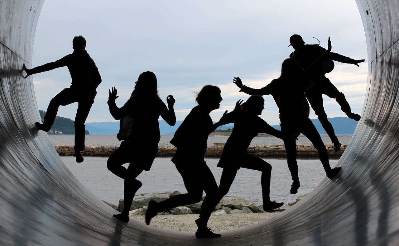 silhouettes of six people running and jumping for fun inside a tunnel. the tunnel is outdoors with a sunny background.