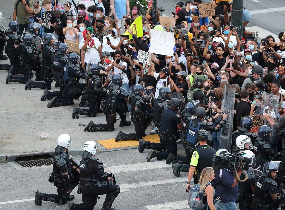 In a show of peace and solidarity, law enforcement officials with riot shields take a knee in front of protesters on Monday, June 1, 2020, in Atlanta