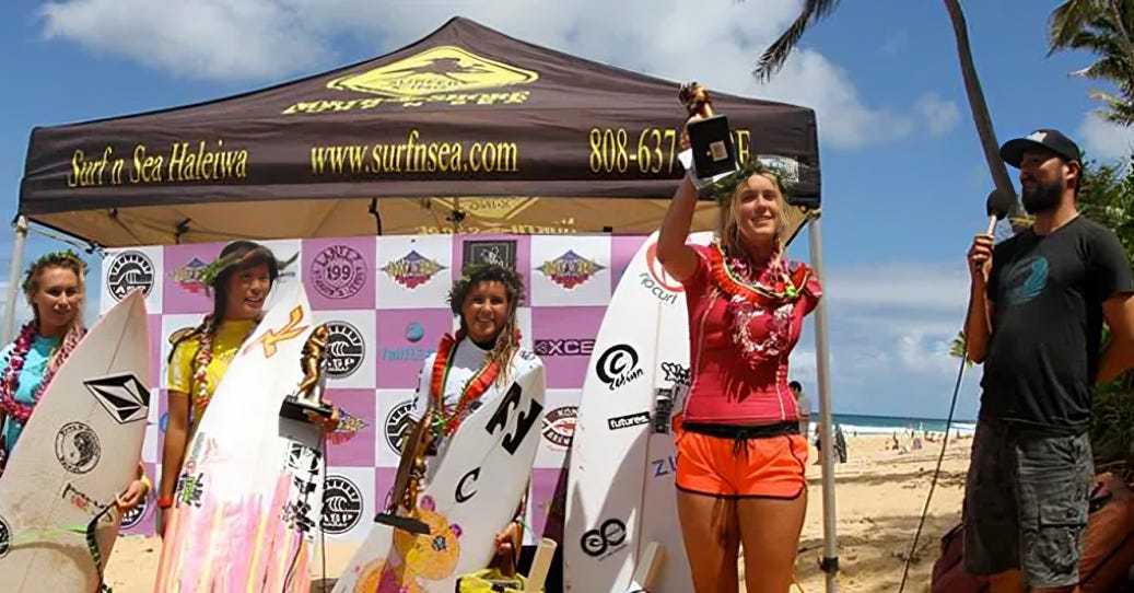 Bethany Hamilton holds a trophy in victory at a surfing competition, standing tall with fellow surfers on the beach, embodying resilience and leadership in women's sports.