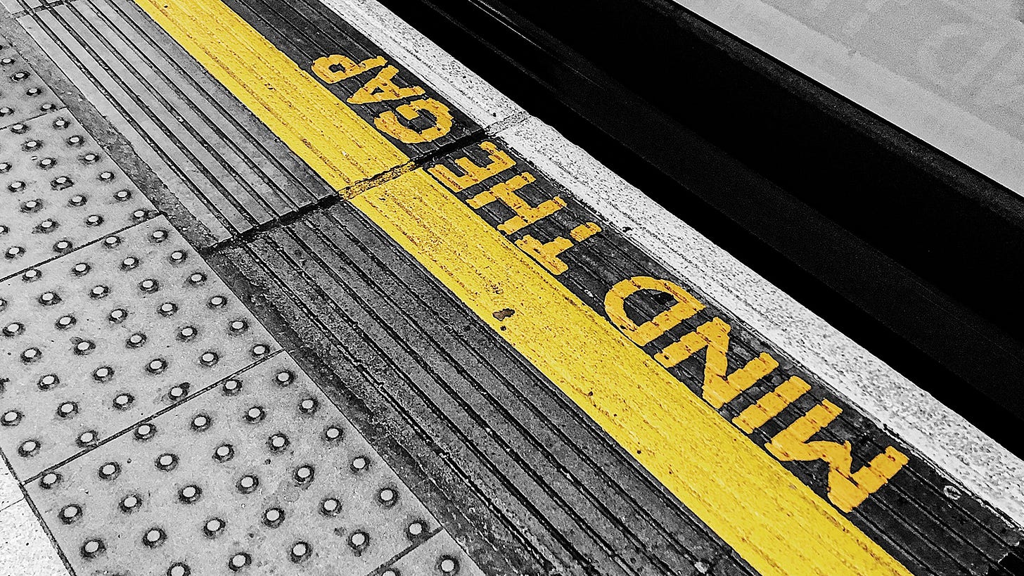 An angled view of a train platform with a line and the words MIND THE GAP in yellow