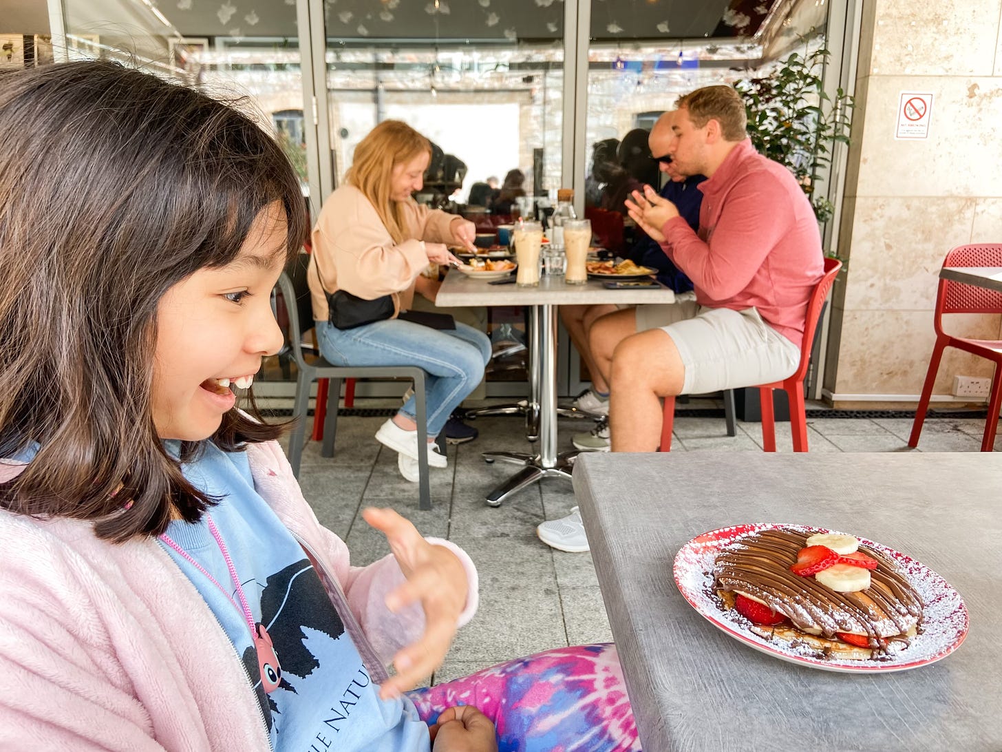 girl with delighted expression, looking at plate of Nutella pancakes on table