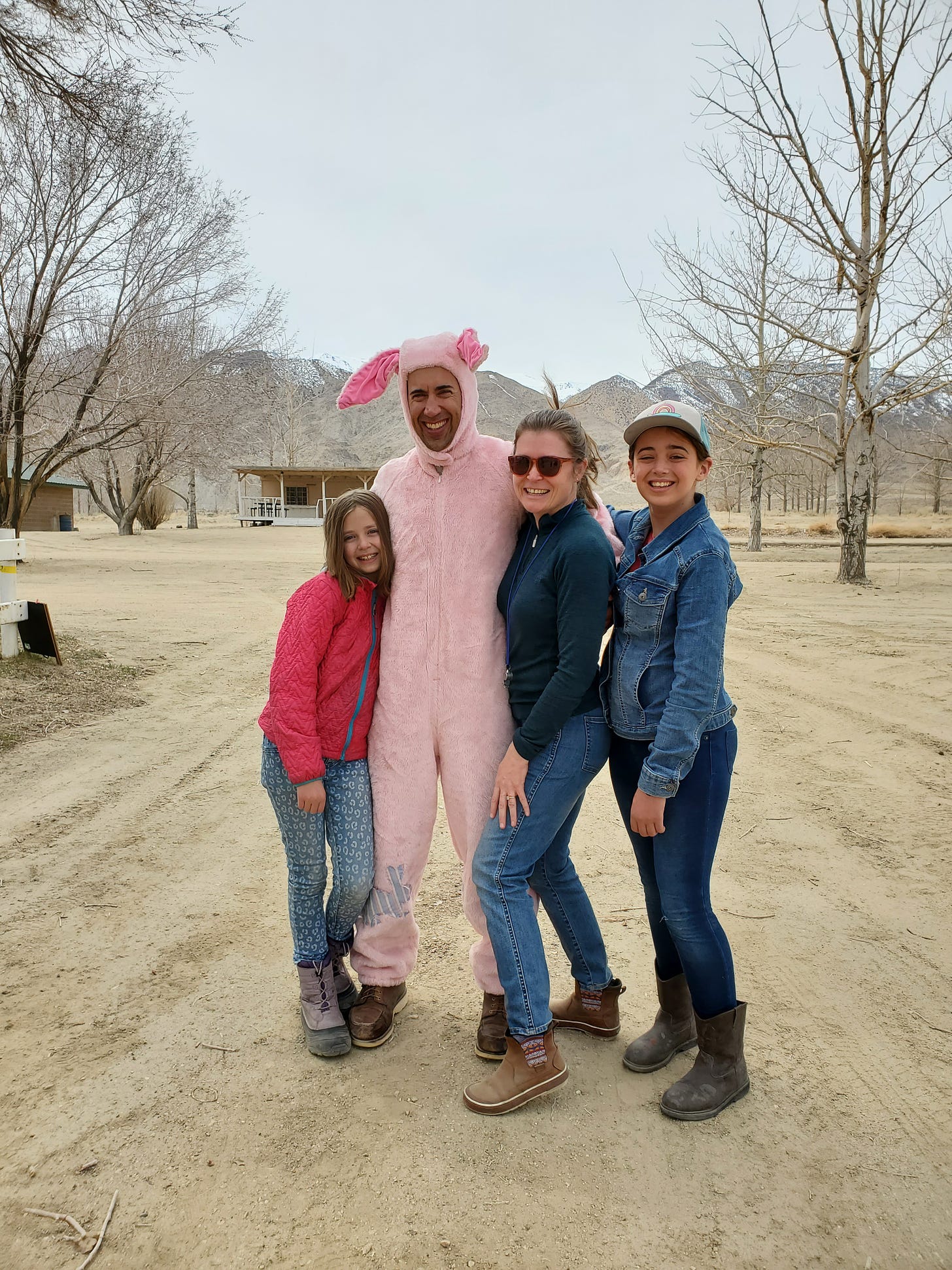 L, Eric, Charlotte, and Cora hugging and smiling at the camera. Eric is in a pink bunny suit.