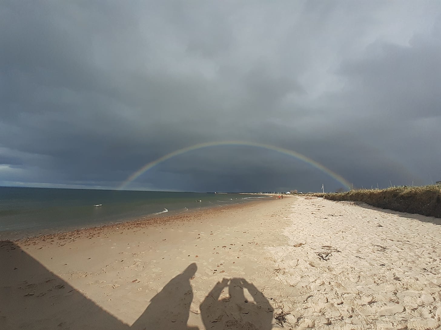 A rainbow strecthing from sea to land looking down Nairn beach with the sea on the left