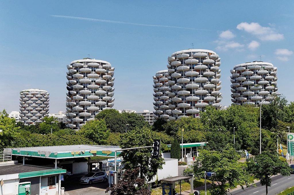 Five of the building towers, with trees in the foreground and a petrol garage