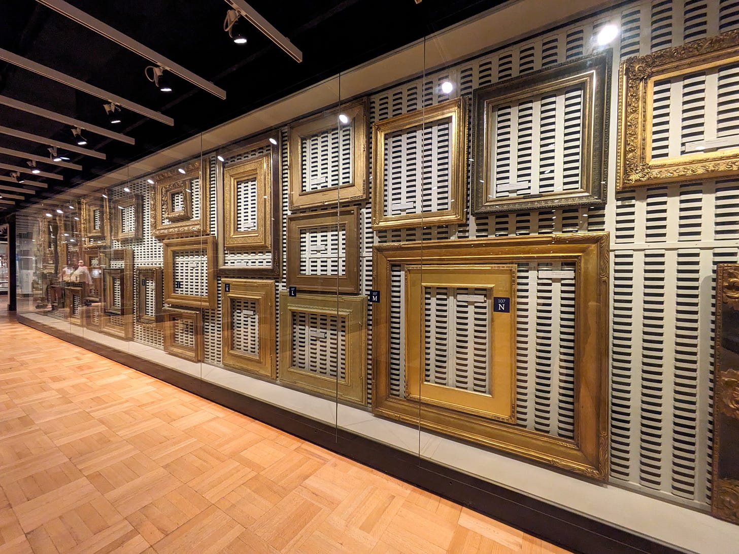 A diagonal view of a large museum case, with several gilded empty picture frames of various sizes and styles.