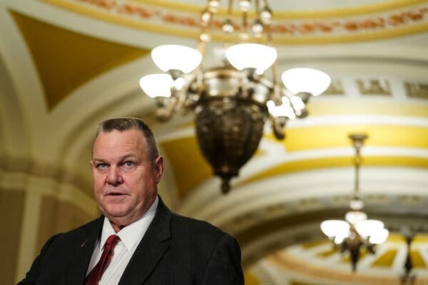 Senator Jon Tester of Montana in a suit with a red tie in the U.S. Capitol.