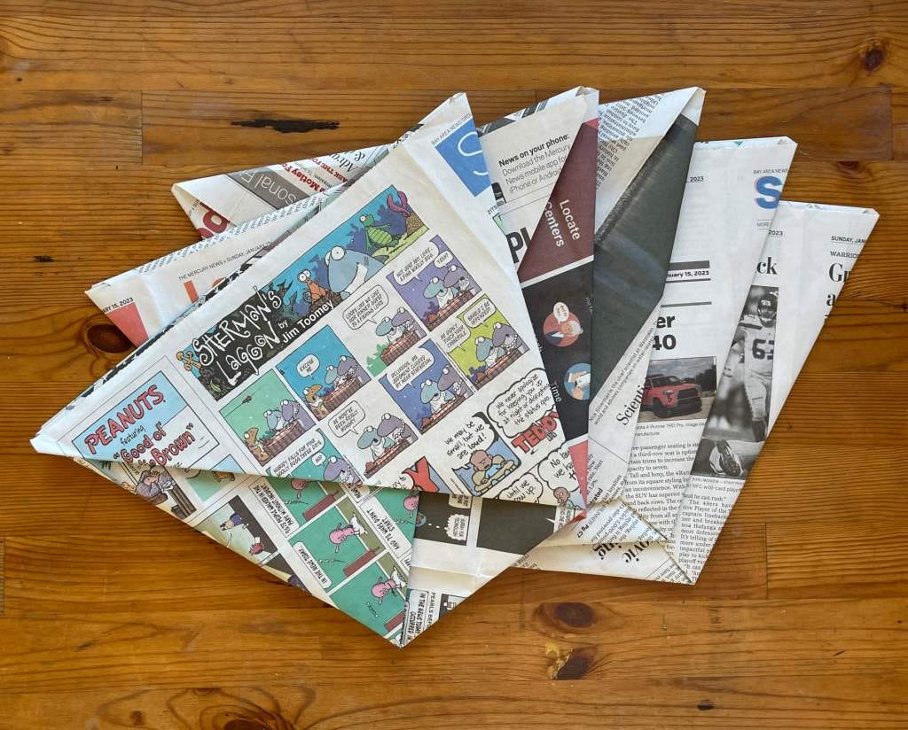 Five compost bin liners made out of folded newspaper sit on a wooden table