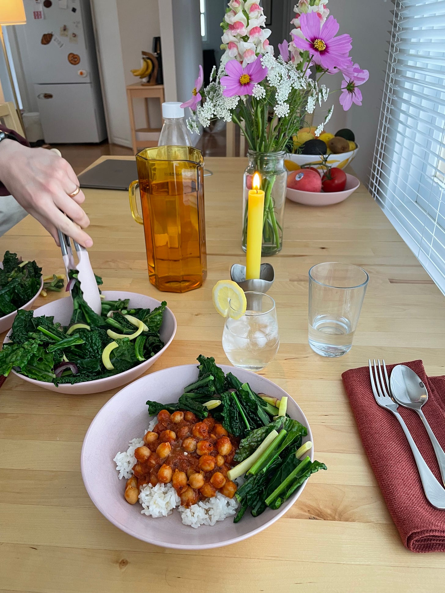 A dining table with flowers and fruit. Two bowls of rice with spiced tomato chickpeas and kale and beans.
