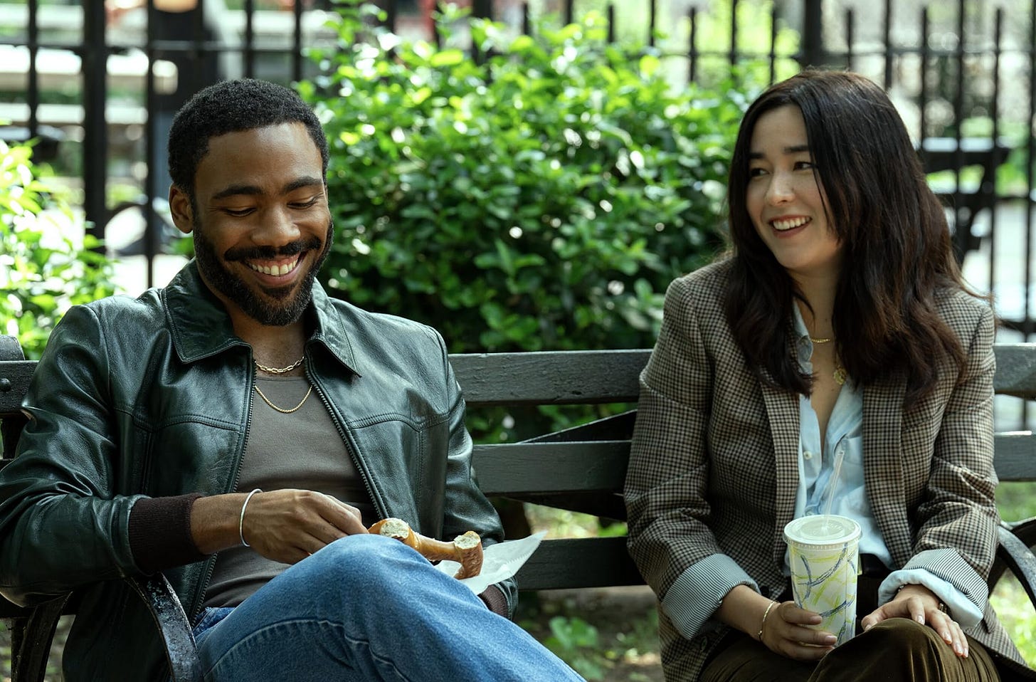 Donald Glover and Maya Erskine as John and Jane Smith, sitting on a park bench together, smiling