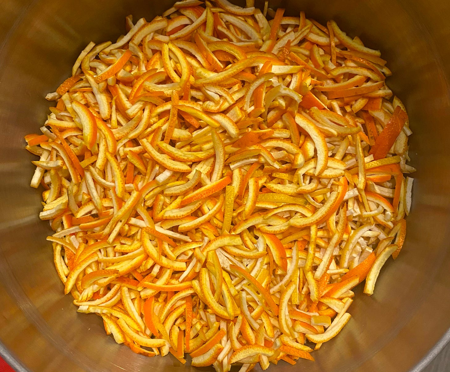 A large steel preserving pan full of finely sliced orange and lemon peel