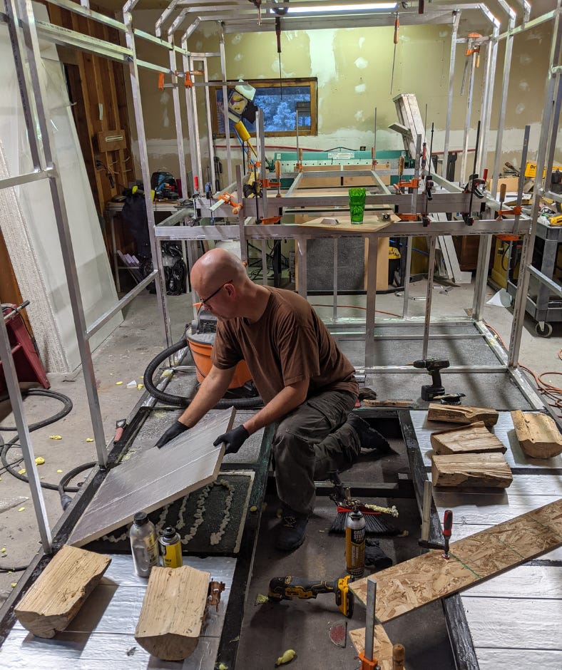 man working in a small barn, surrounded by the metal ribs that will become the camper