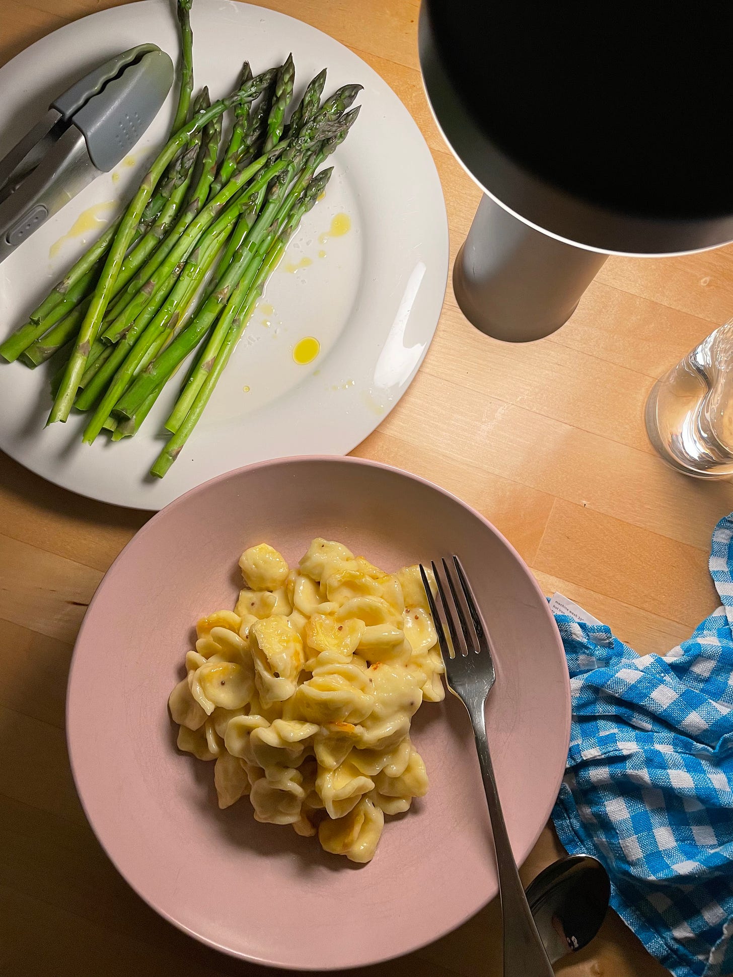 Bowl of orecchiette pasta in a cheesy sauce, with a plate of steamed asparagus topped with olive oil alongside.