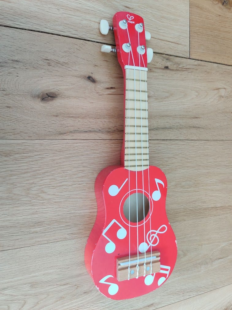 Red toy ukulele lying on a wooden floor
