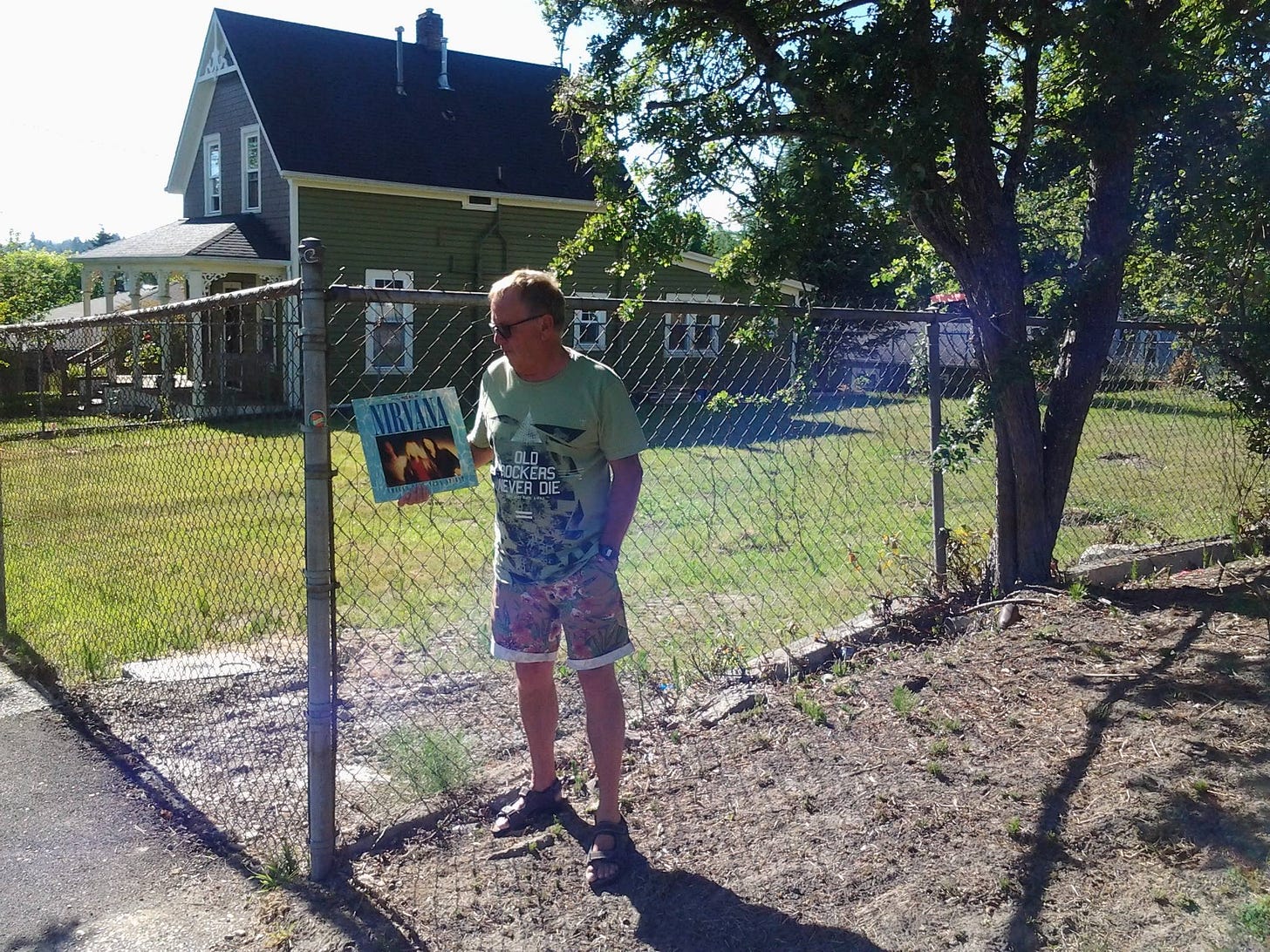 A man standing in front of Kurt Cobain's house with an EP in hand.