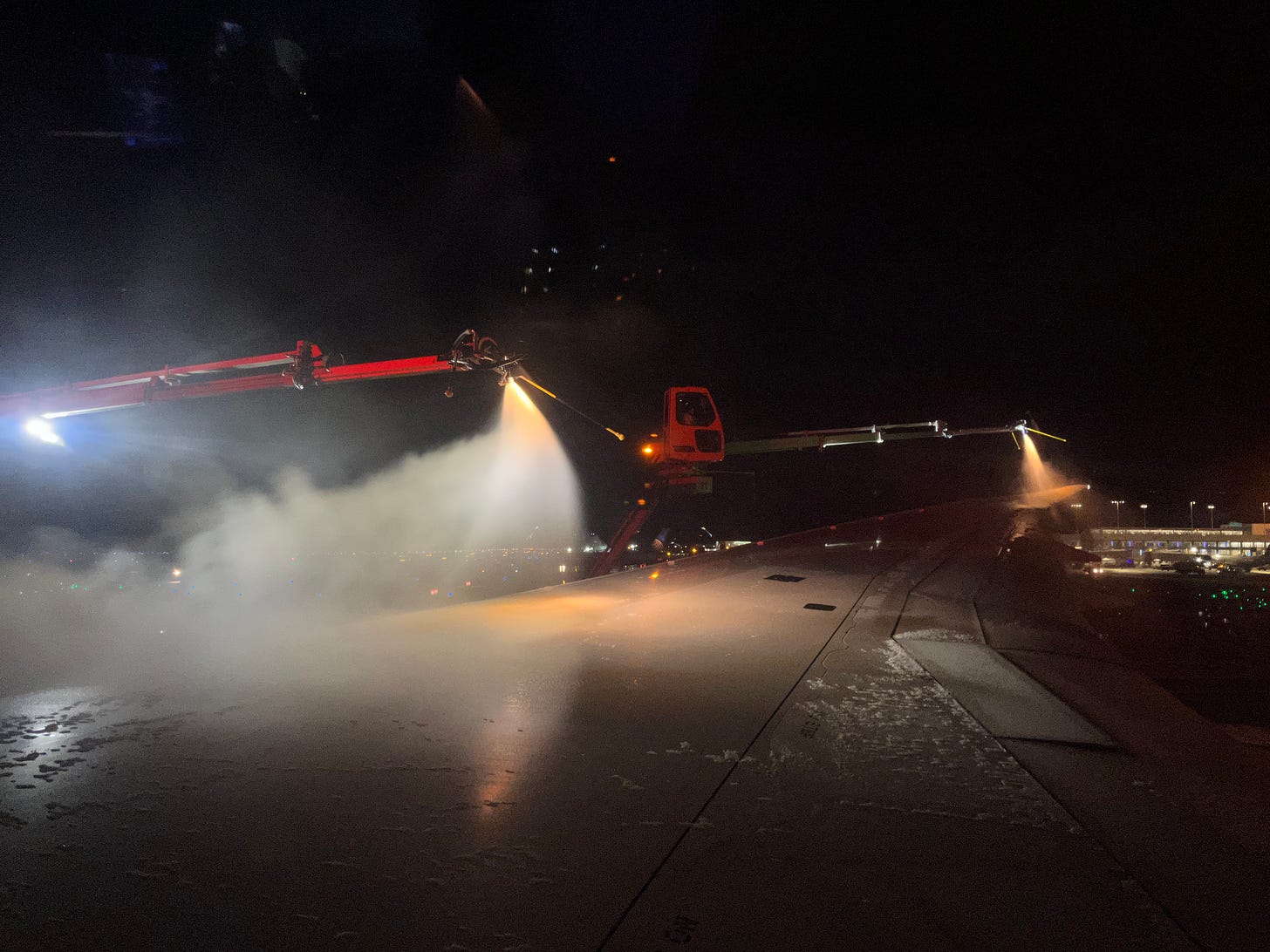 photo of the wing of a 787 airplane at night with two deicing machines spraying it