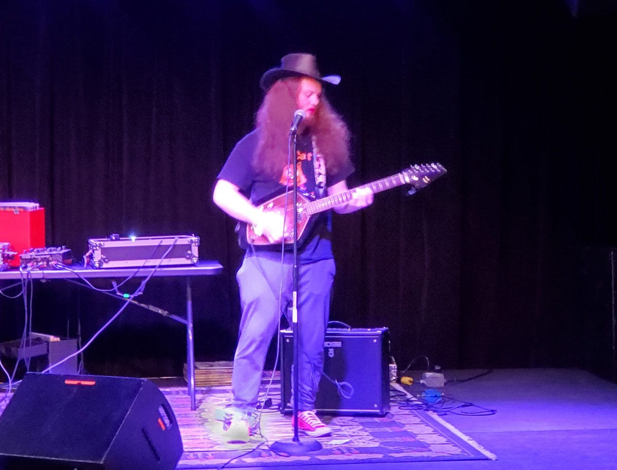 man with long hair plays guitar on stage