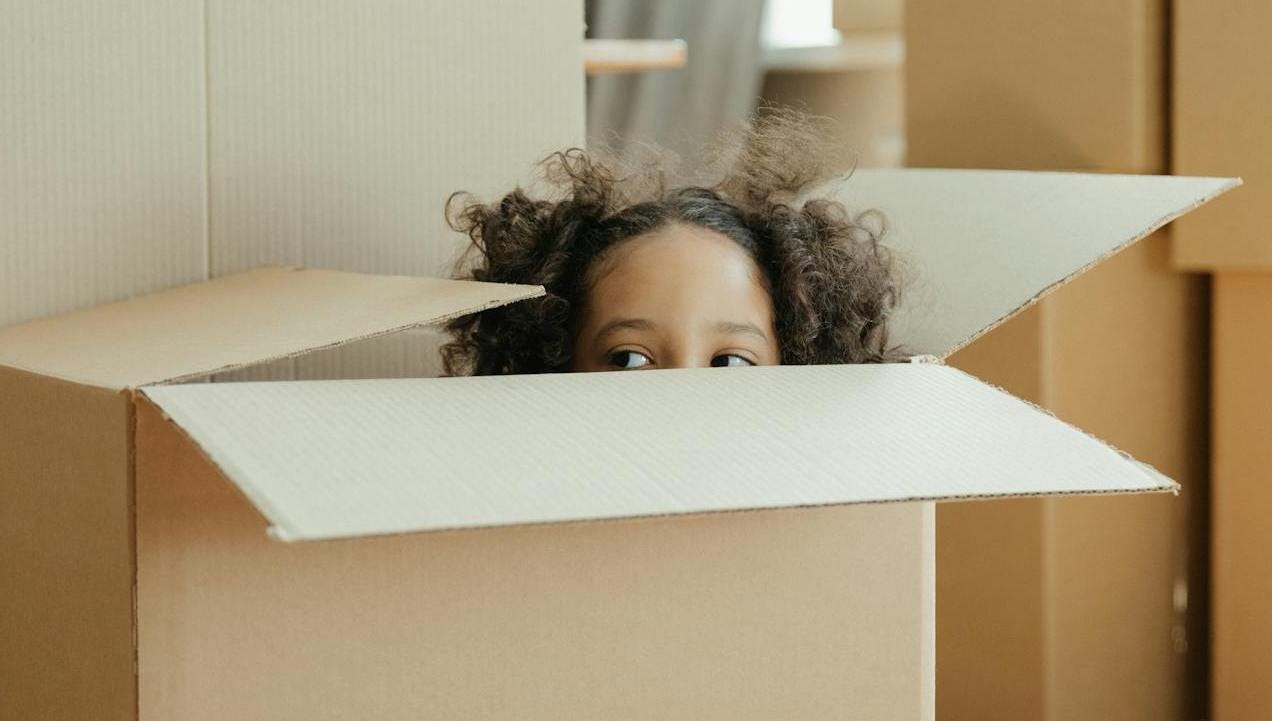 A girl peaking out of the top of an open cardboard box. A girl peaking out of the top of an open cardboard box.