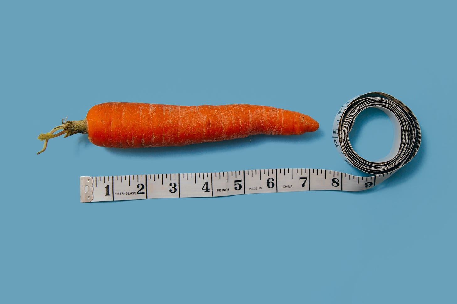 Photo of a carrot and measuring stick on a blue surface