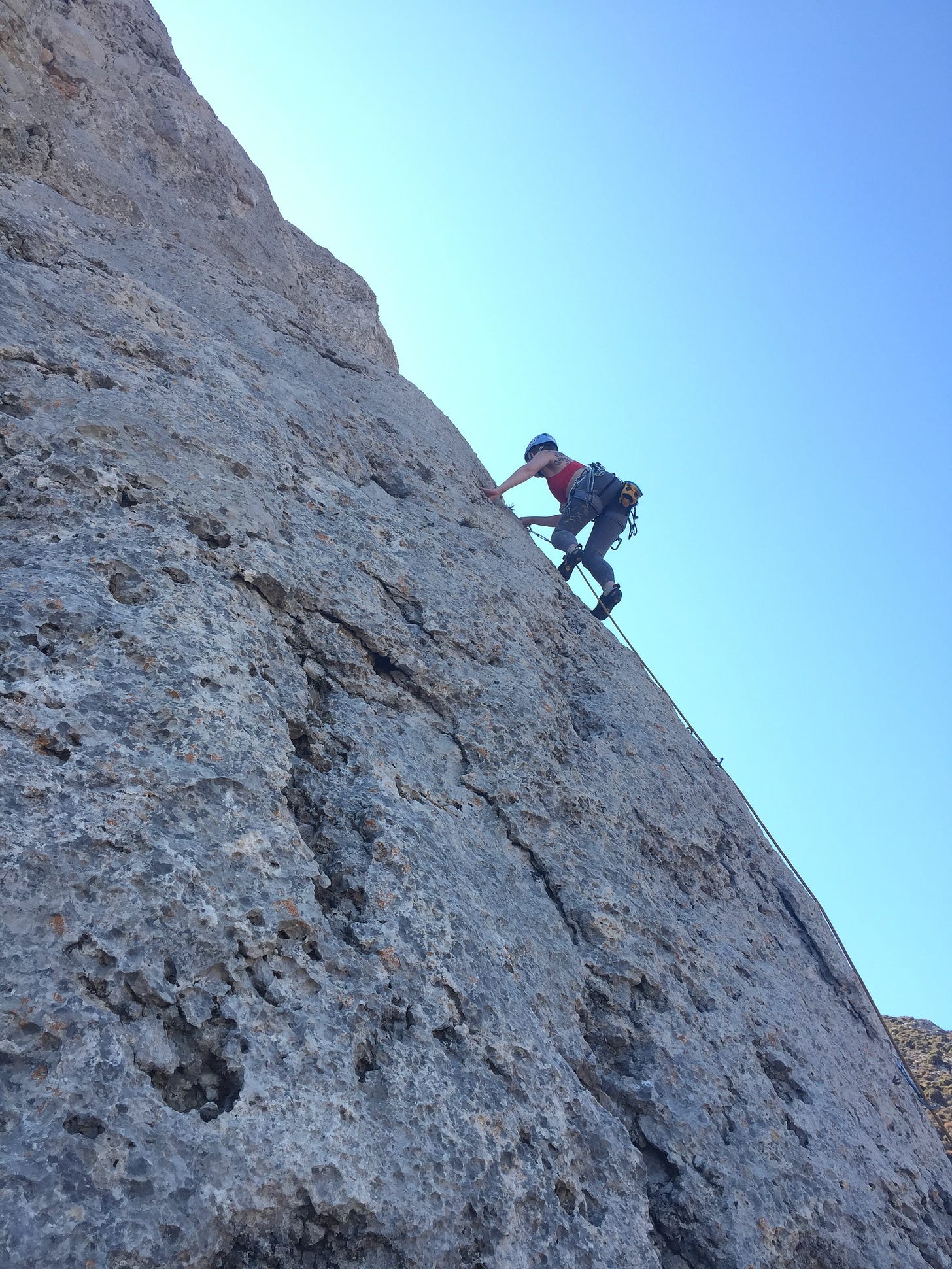 Vicky on a very steep rock face in Kalymnos, blue sky behind, climbing with ropes.