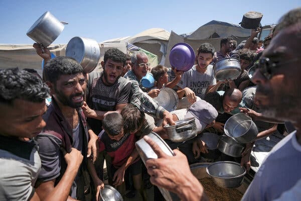 A crowd of people, many holding empty pots or bowls, shout and push each other Friday at a food distribution center in central Gaza. 