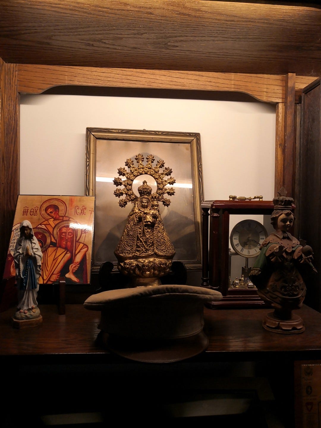 A picture of religious imagery, an antique clock, and an officer's cap.
