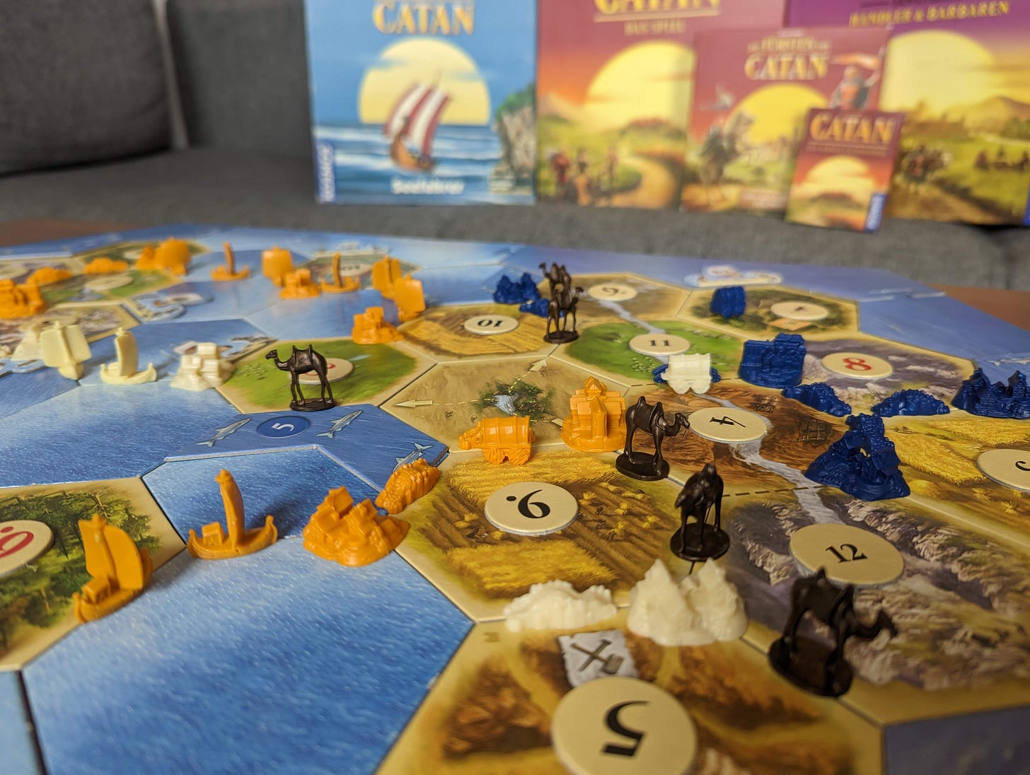 Ein Catan-Spielfeld mit Schiffen auf Meerfeldern, Kamelen aus der Oase, Trosswägen, Fischgründen und Brücken über Flüssen.