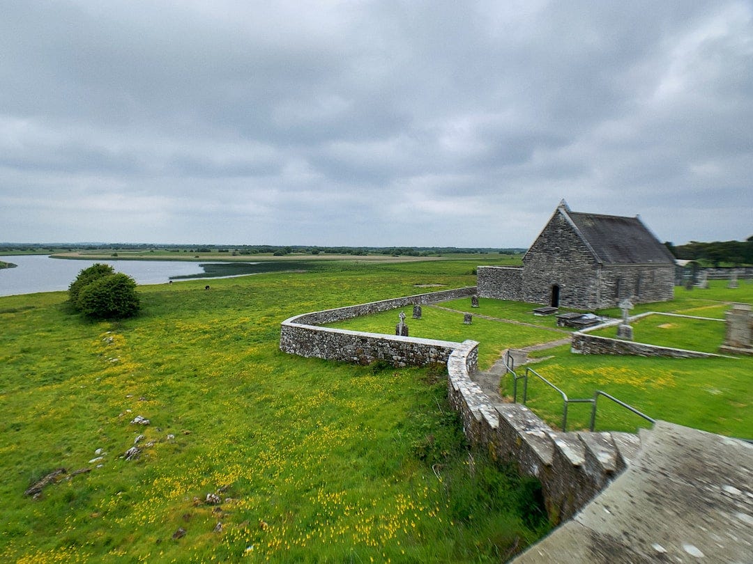 a stone building with a grass field and a body of water in the background