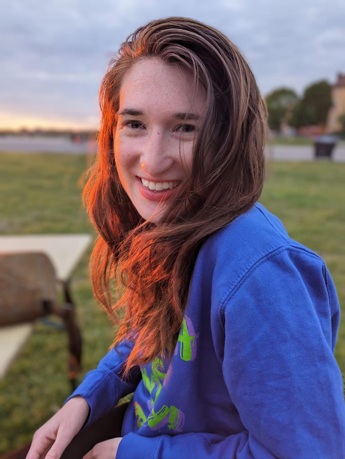 A portrait of Laney wearing a blue sweatshirt. She is smiling, and the sun lights up one side of her face.