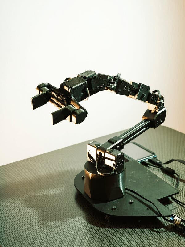 A close-up view of a single robot arm, bent at one of its joints, that stands upright from a black metal base on a tabletop.