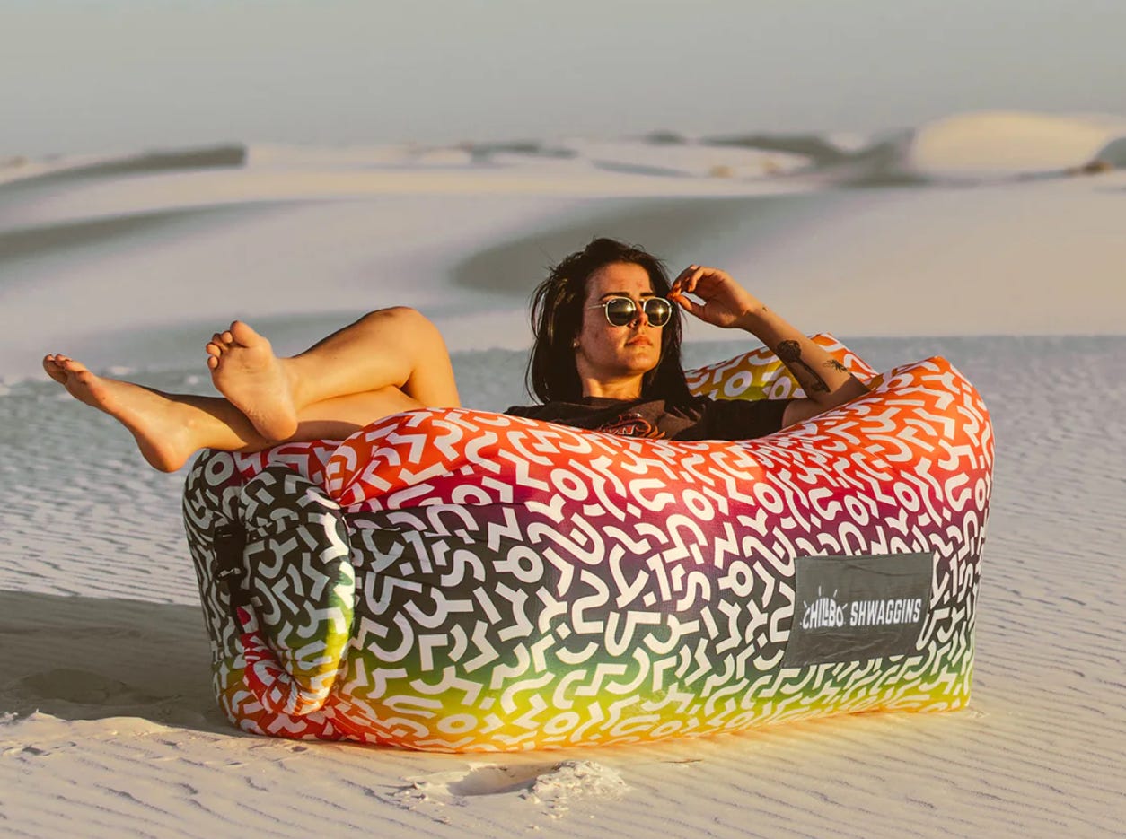 A white woman looking moderately comfortable lying inside an inflatable hot-dog-shaped lounger on a beach