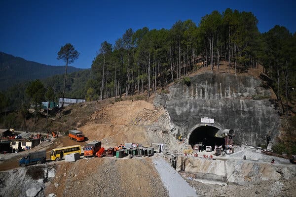 A tunnel mouth with vehicles and equipment nearby. It’s on a face of sheer rock sliced into a wooded hillside.