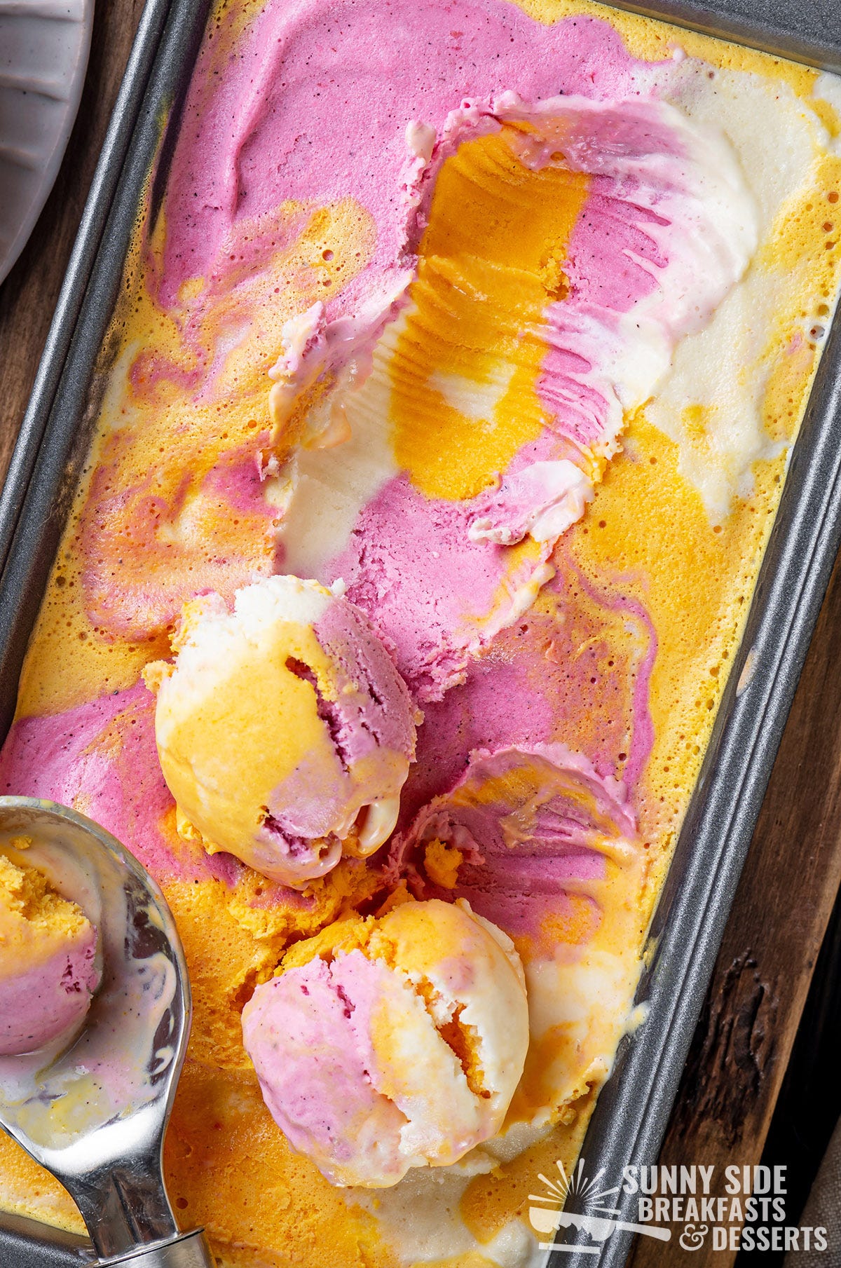 Scooping homemade rainbow sherbet in a loaf pan.