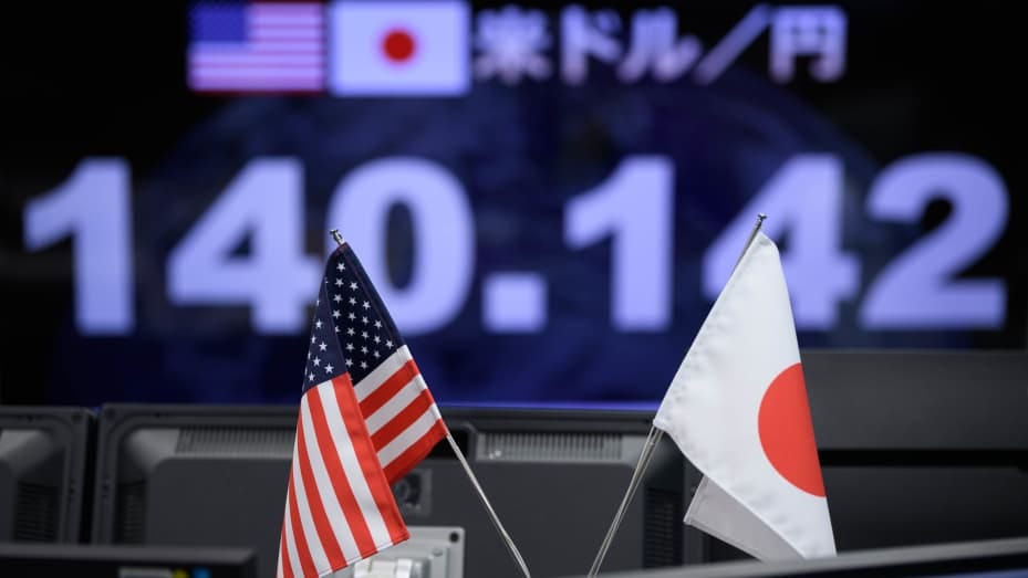 The U.S. and Japanese flags in front of the yen-dollar exchange rate in the trading room at foreign exchange brokerage Gaitame.Com Co. in Tokyo, Japan, on Friday, Sept. 2, 2022.