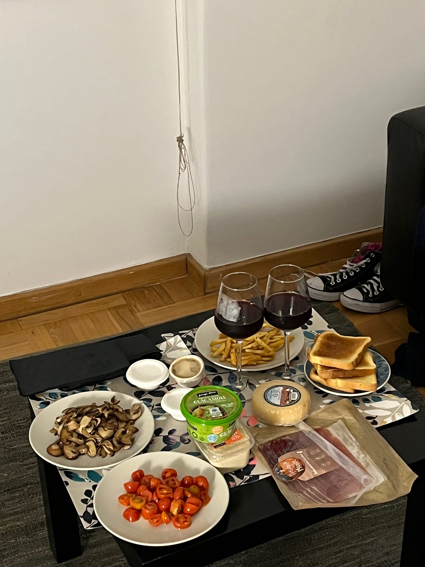 Jantar improvisado no chão da sala do nosso airbnb em Lisboa: tomatinhos, cogumelos, pão, queijos, duas taças de vinho, hommus e guacamole