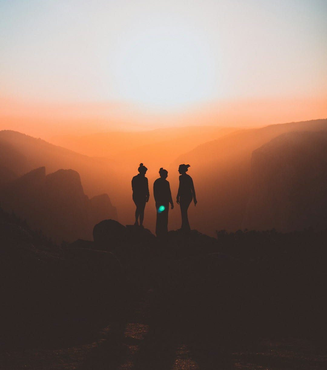 silhouette of three people up on mountain cliff