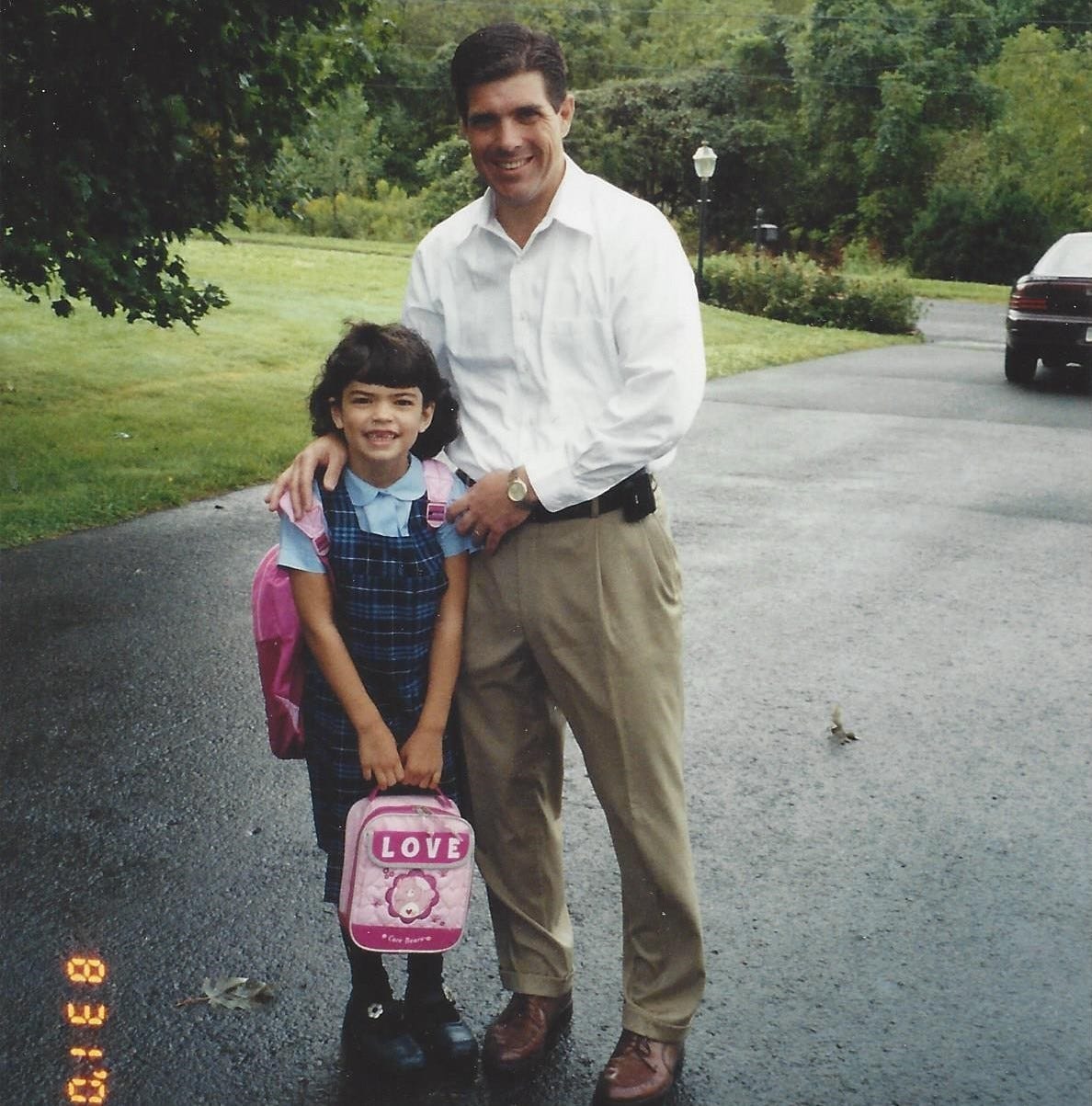 Dad posed alongside his daughter on her first day of first grade. A portion of a purple Dodge Intrepid can be seen in the background