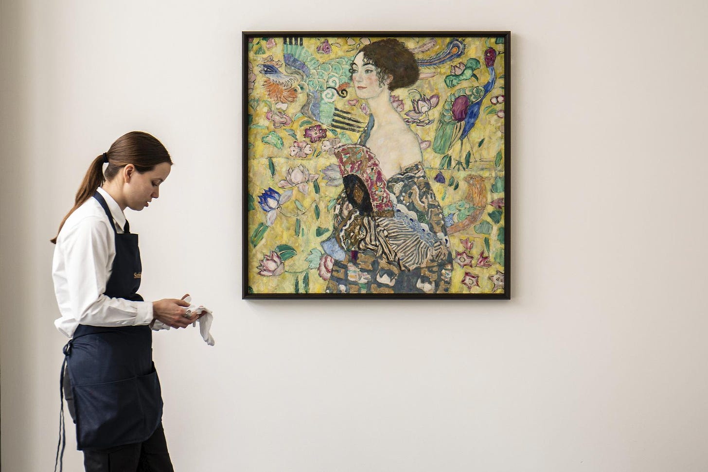 a woman stands next to Gustav Klimt's painting of Lady with a Fan